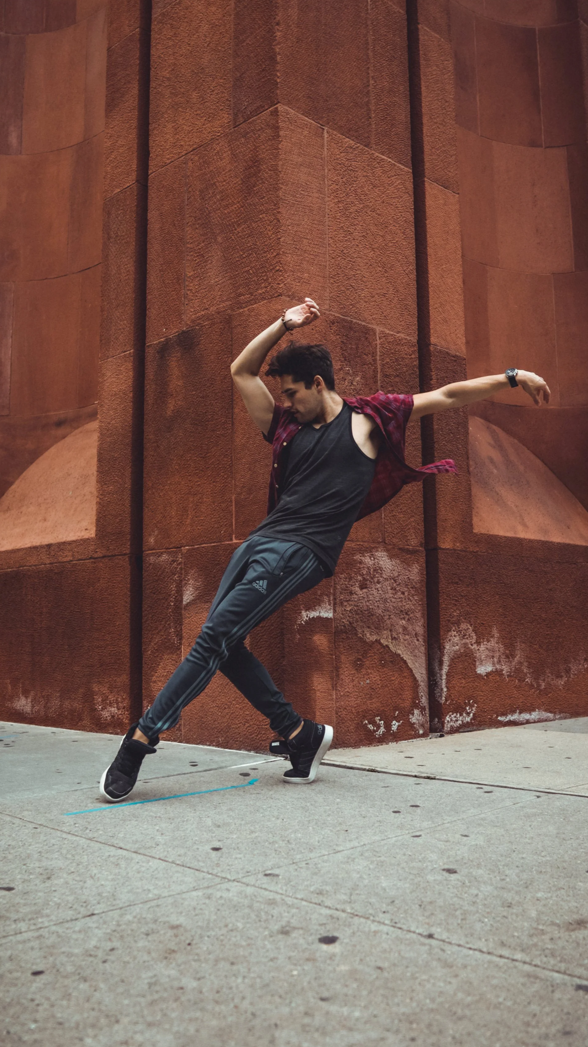 A young man performing a dance move on the sidewalk in front of a large reddish-brown building.