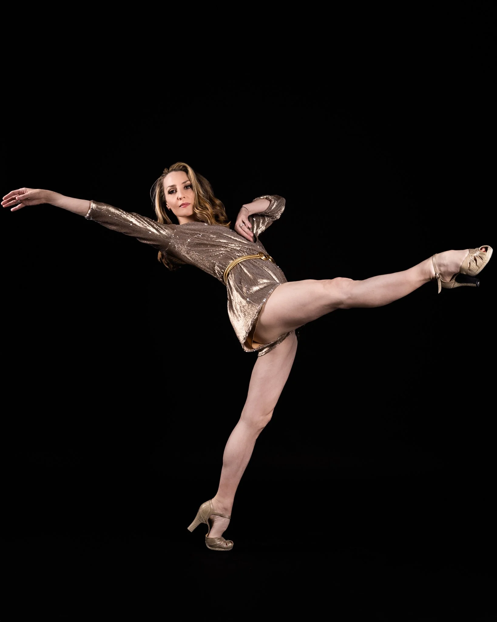 A woman dressed in a gold, sequined dress performs a dance or gymnastic move.