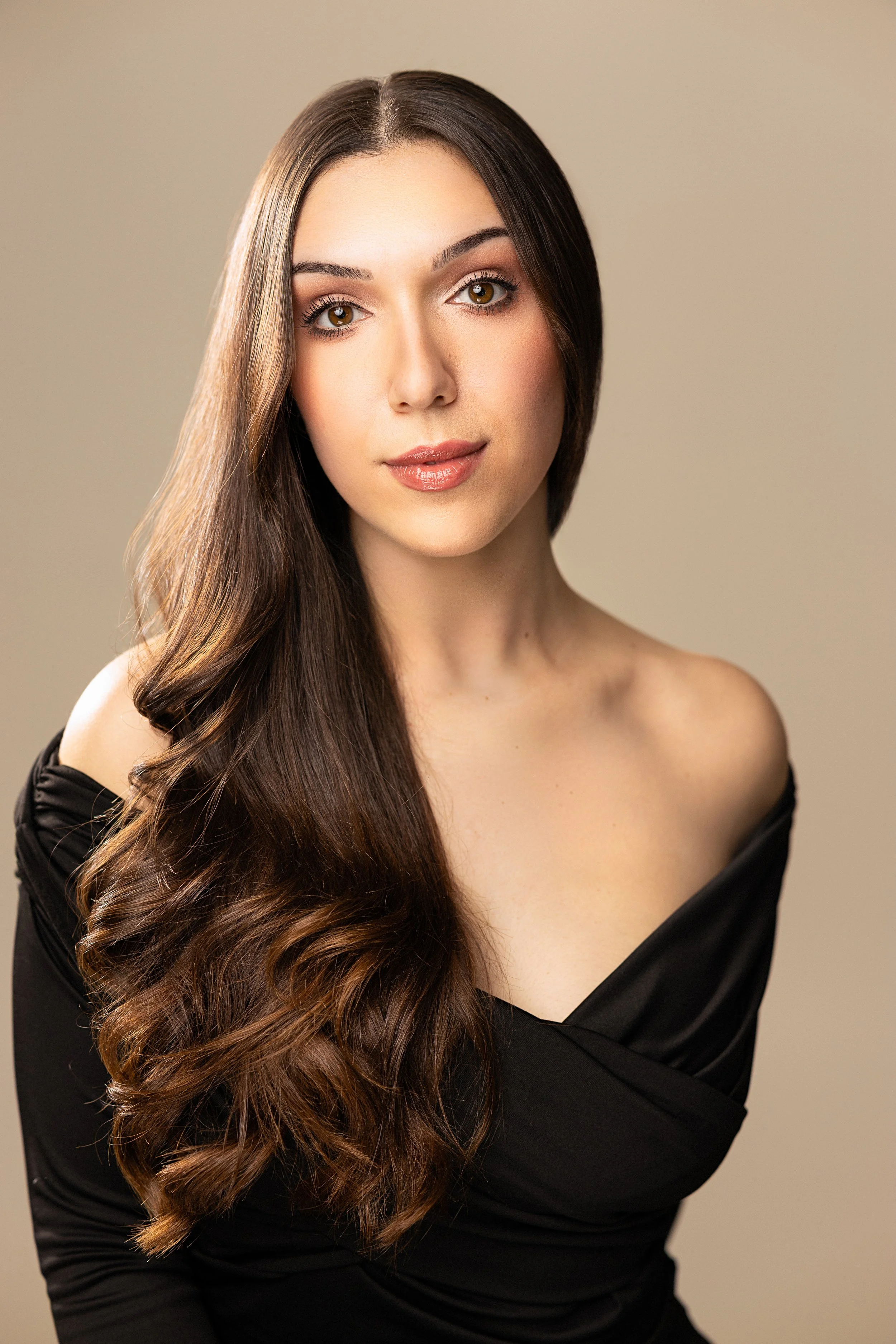 Portrait of a young woman with long, wavy brown hair, wearing an off-the-shoulder top.