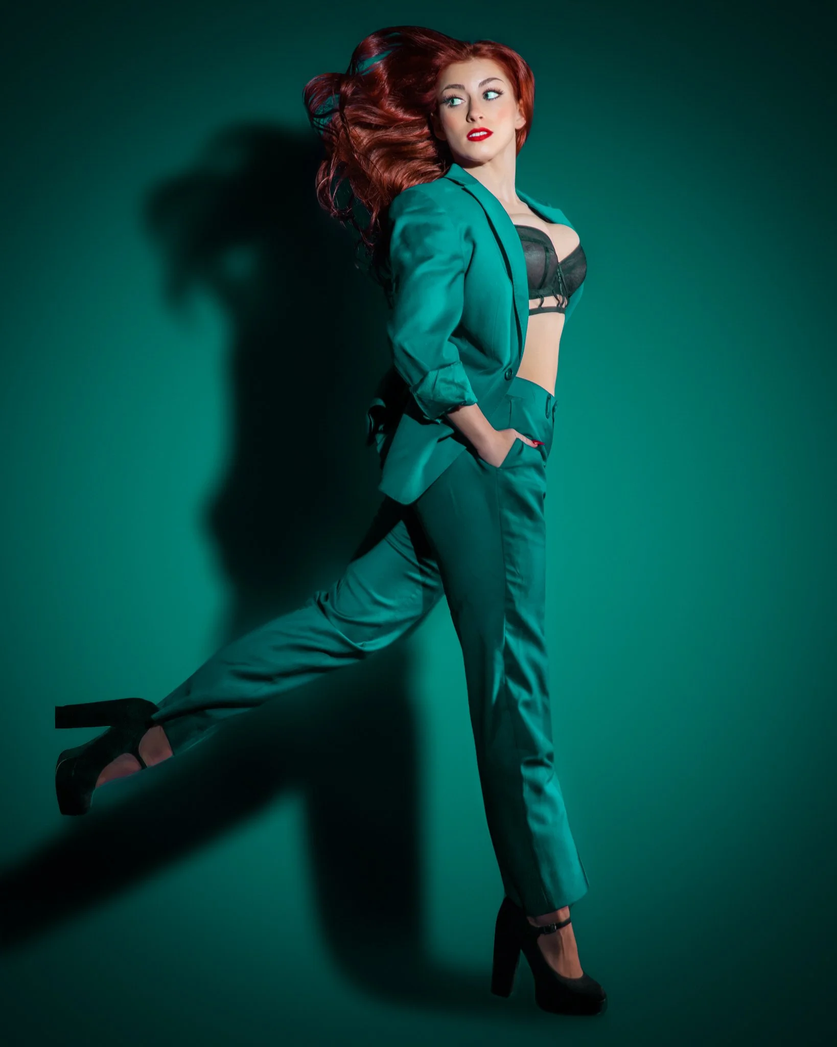 Woman with long red hair wearing a teal blazer and matching pants, black bra.