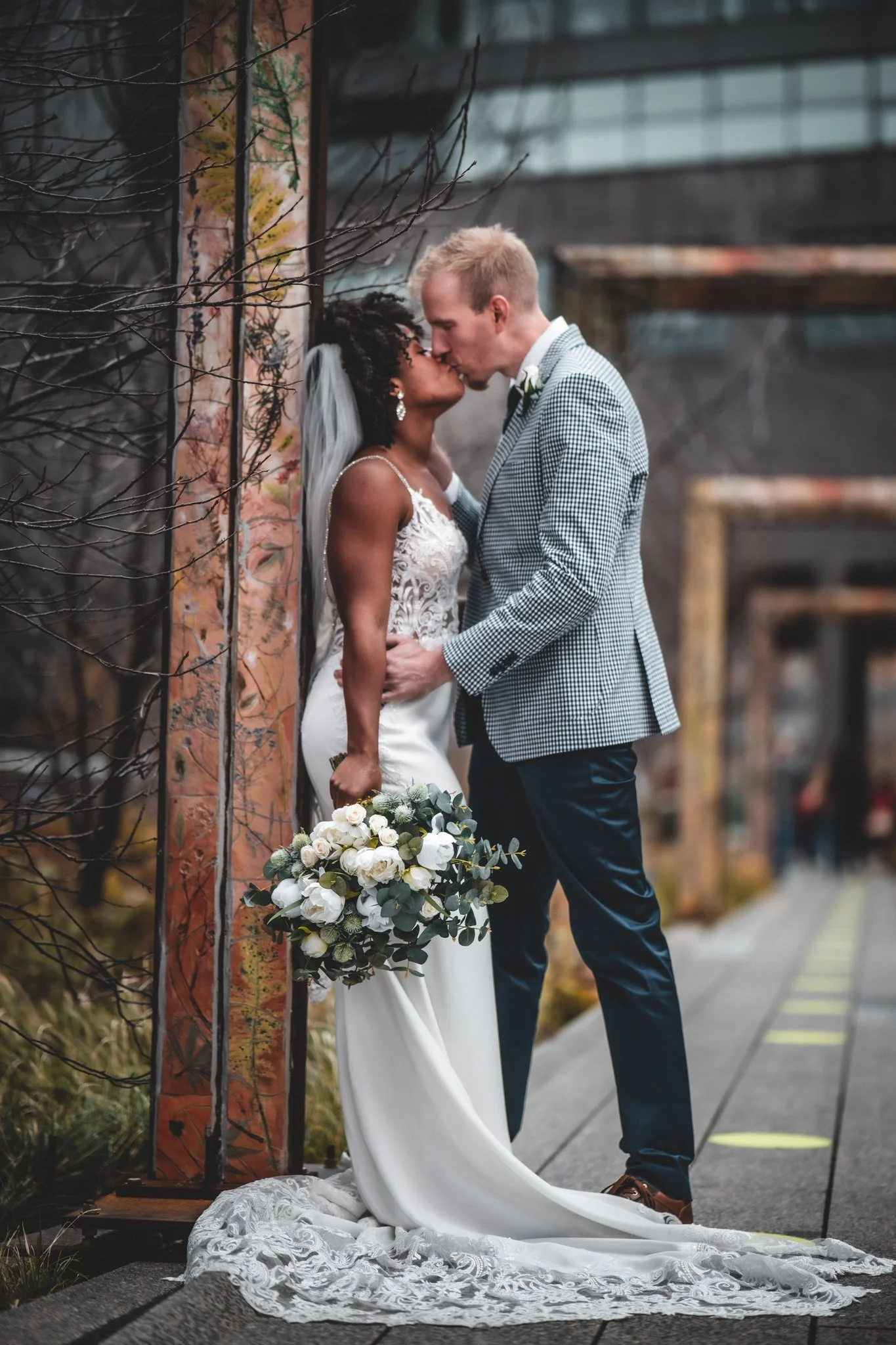 A newly married couple sharing a kiss outdoors, with the bride holding a bouquet.